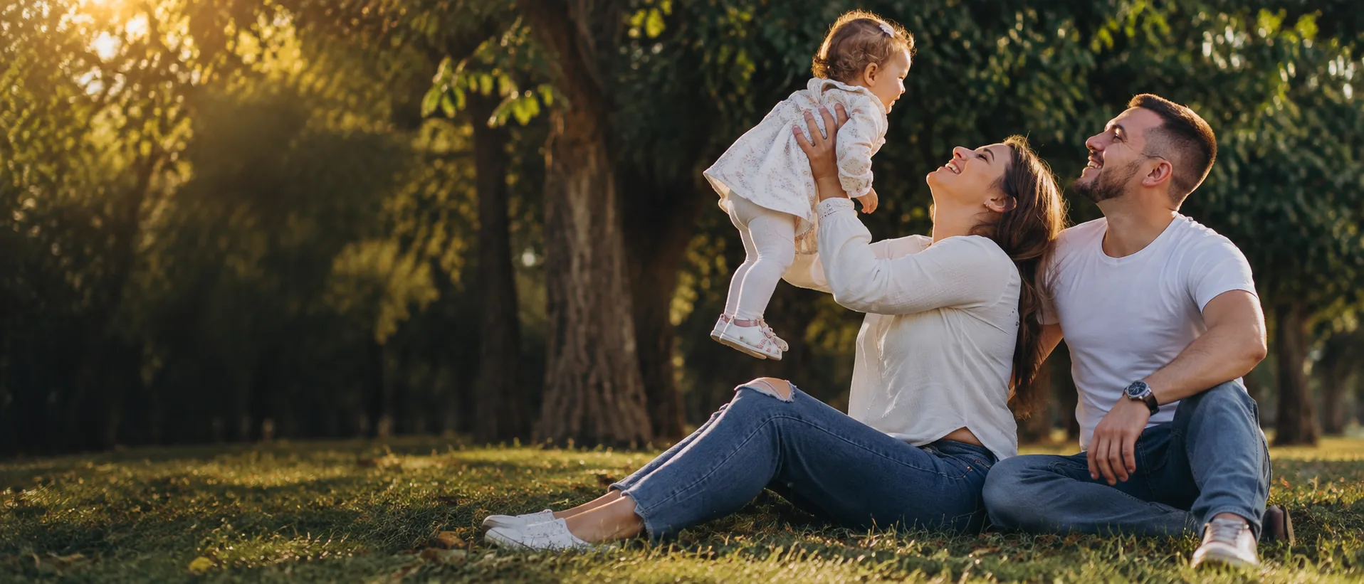 Família em um parque, com uma criança nos braços da mãe e o pai ao lado